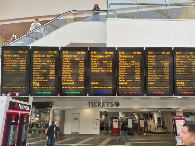 A train departures board shows service information for routes to Birmingham airport.