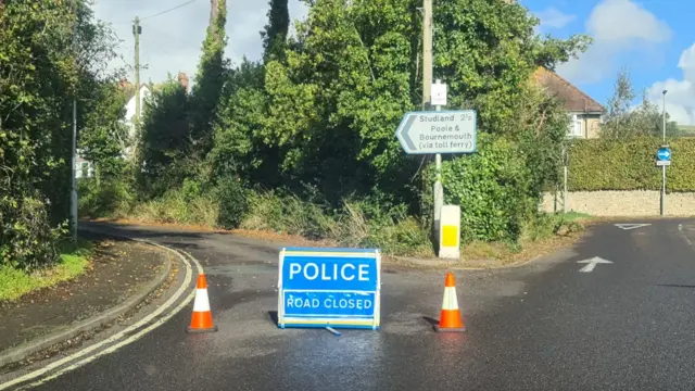 A police road closed sign with two cones blocks off an entrance to Ulwell Road