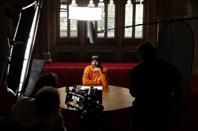 Tyson Fury speaks in a room surrounded by cameras