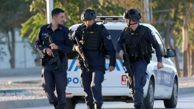 Three armed police walk close to the scene