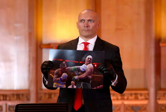 Oleksandr Usyk poses with a picture of him punching Tyson Fury, signed by Tyson Fury