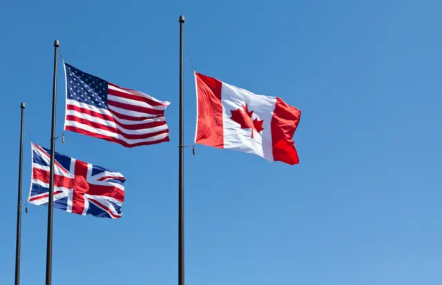 American, British and Canadian flags are waving in a blue sky