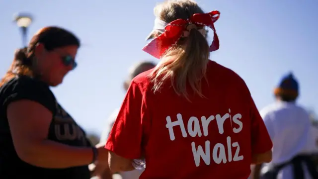 A woman wears a red shirt with the words Harris Walz on it