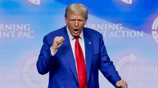 Donald Trump, in blue suit, white blouse and red tie, punching the air at a rally in Duluth, Georgia. He sports an American flag pin on the left lapel of his jacket