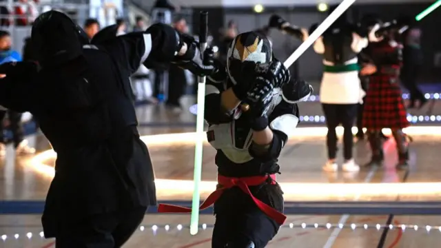 Two duelists wearing movie-style protective gear fight with lightsabers