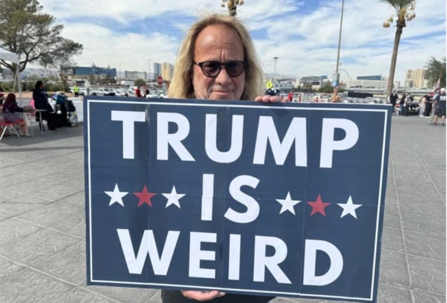 Don Gold stands with a sign that reads "Trump is weird"