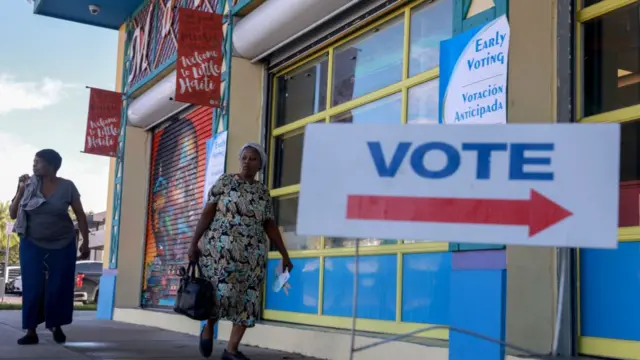 Two voters arrive at the Little Haiti Cultural Complex to cast their ballots in Miami, Florida - there is a large 'vote' sign with an arrow pointing right