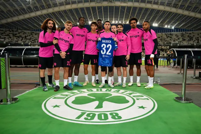 Players of Chelsea, hold a shirt which reads "Baldock, 32" in remembrance of Panathinaikos FC player George Baldock, who recently passed away