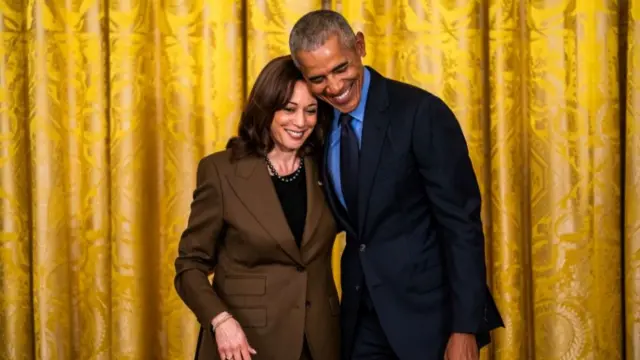 Former President Barack Obama and Vice President Kamala Harris embrace in front of a golden curtain in the East Room of The White House