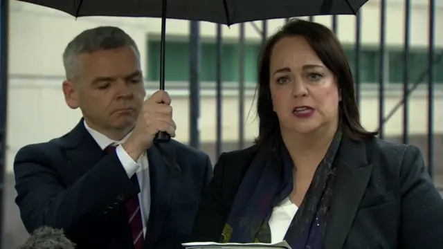 Catherine Kiernans outside court. She is wearing a black suit and standing under an umbrella.