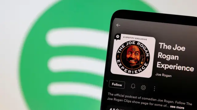 Joe Rogan's Spotify profile is seen in front of displayed Spotify logo