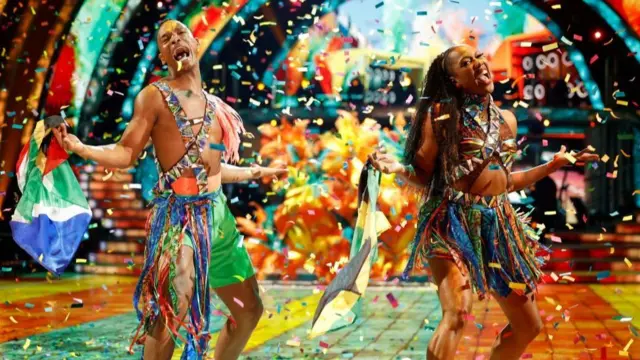 Montell Douglas and Johannes Radebe dancing their carnival-inspired couple’s choice, Johannes holding a South African flag and Montell holding a Jamaican flag,  with multi-coloured confetti surrounding them on the dancefloor.