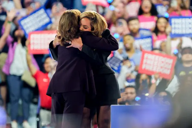 Beyoncé and Harris hug on stage while supporters waves signs in the background