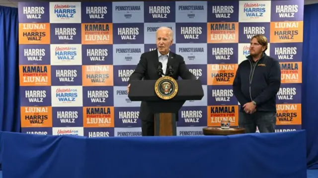 Biden speaks at a lectern in front of Harris-Walz signs