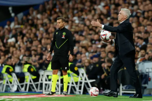 Ancelotti waves his hand while carrying the ball back to the pitch