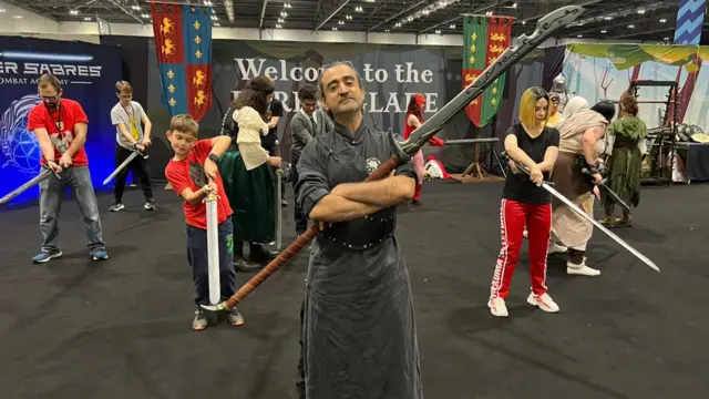 Faisal Mian holding a long spear while standing before a group of students