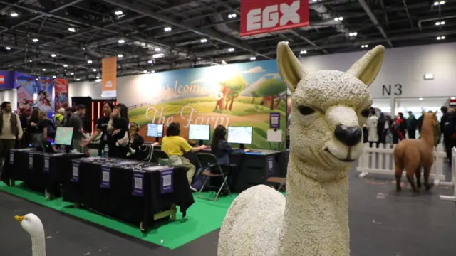 A llama and a goose in the foreground, with people playing video games in the background