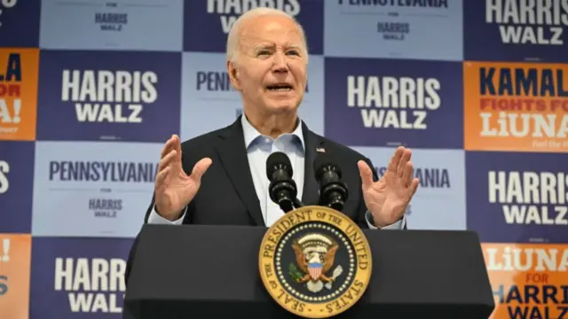 Biden speaks at a podium in front of Harris-Walz signs