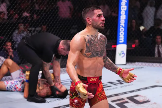 Ilia Topuria celebrates with Max Holloway on the floor behind him