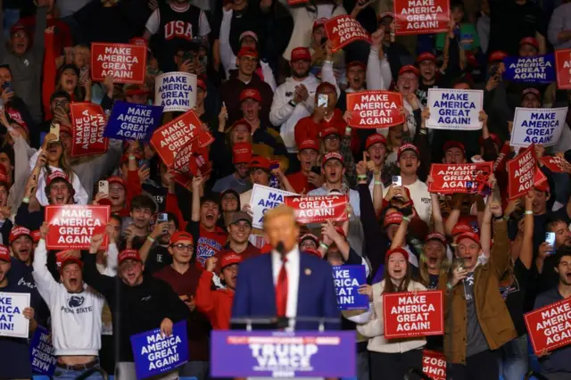 Trump speaks in front of a crowd waving Trump signs