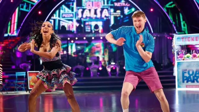 Jamie Borthwick and Michelle Tsiakkas mid-dance with lights and a 'ticket' machine seen in the background of the stage