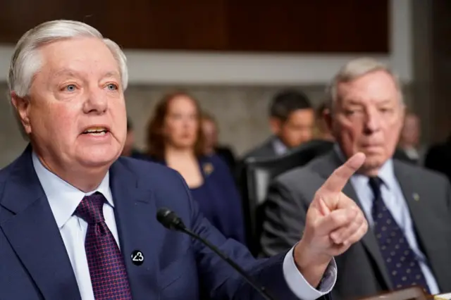 Lindsey Graham gestures with his index finger held up while speaking at a microphone