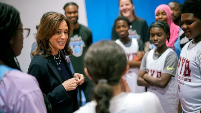 Kamala Harris speaks with youth basketball players, she wears a black suit and the children wear basketball jerseys.