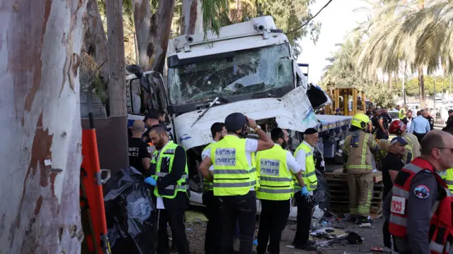 Image shows the front of a lorry with a smashed windscreen, with emergency personnel in hi-vis working at the scene