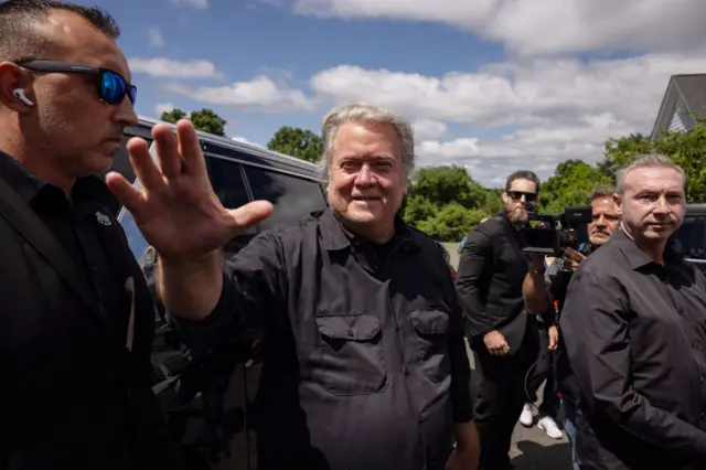 Bannon waves his right hand while flanked by two security guards