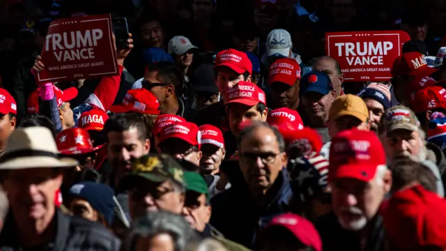 A photo taken from above of a crowd of people wearing red Trump merchandise feature slogans including 'Trump Vance Make America Great Again'