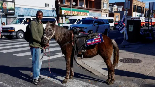 A man stands with a horse sporting a sign reading 'Philly for Kamala'