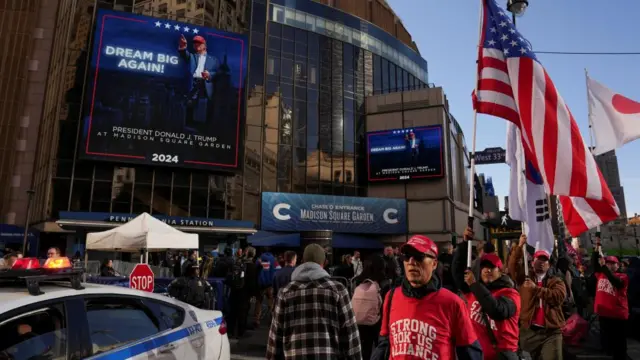 People dressed in red MAGA hats hold American flags and line up outside of Madison Square Garden