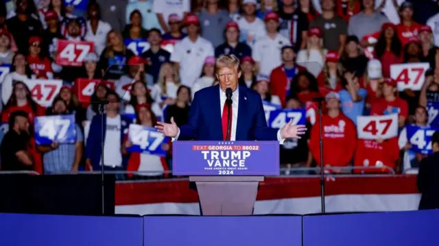 Donald Trump speaking to supporters at a rally in Atlanta, Georgia, before a podium with a plaque that reads 'Trump Vance 2024'