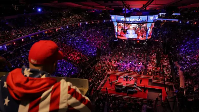 A man in a top designed to look like a US flag watches on as thousands listen to Trump speak at Madison Square Garden