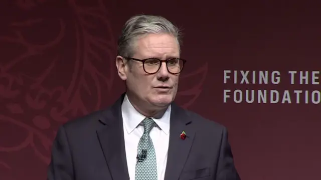 Keir Starmer delivers speech in black suit, white shirt and turquoise patterned shirt