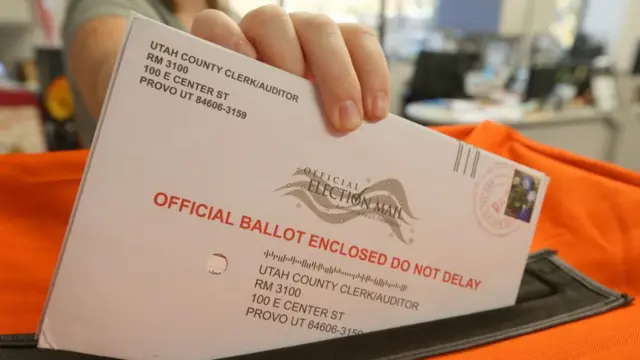 Close-up of a voter's fingers dropping a mail ballot into a drop box in Utah