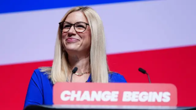 Ellie Reeves grins as she stands behind a lectern bearing the phrase 'change begins'