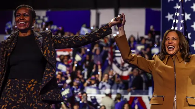 Kamala Harris and former First Lady Michelle Obama hold hands as they attend a campaign event for Harris at Wings Event Center in Kalamazoo, Michigan