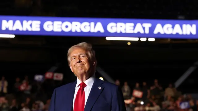 Donald Trump stands in front of a sign saying "make Georgia great again" at a rally