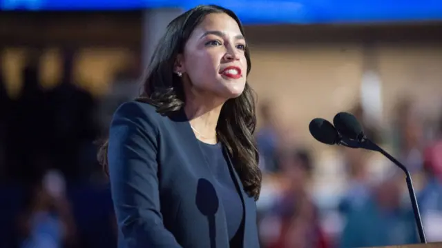 Alexandria Ocasio Cortez speaks at a microphone