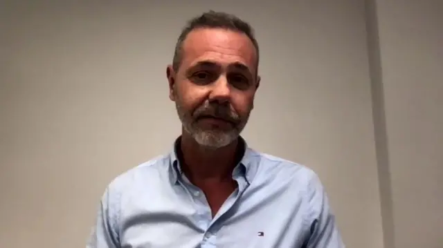 Nick Grey headshot, wearing a blue shirt in front of a white wall