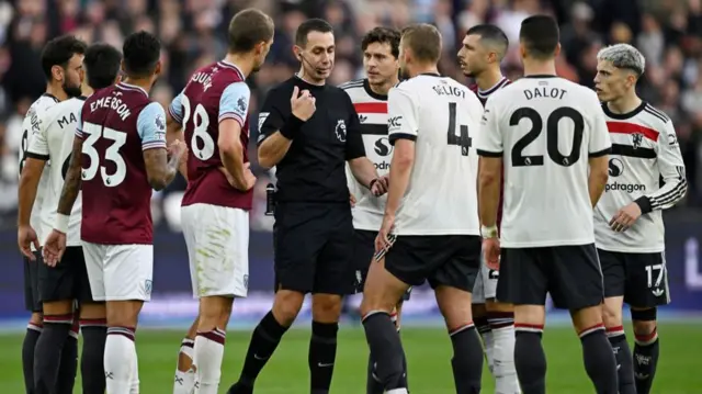 Referee David Coote speaks to West Ham and Manchester United players as they wait for a penalty decision