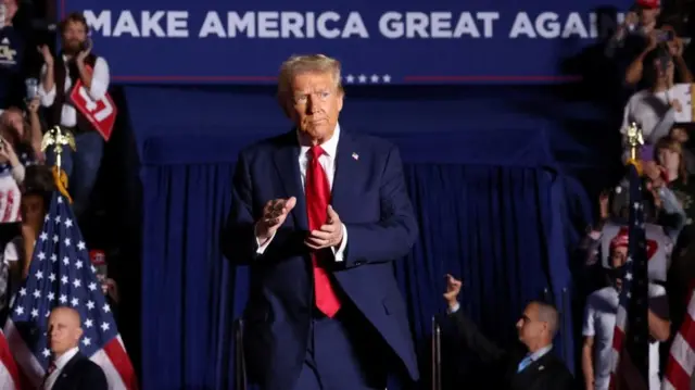 Donald Trump clapping as he enters a rally in Atlanta, Georgia, with a 'Make America Great Again' banner behind him