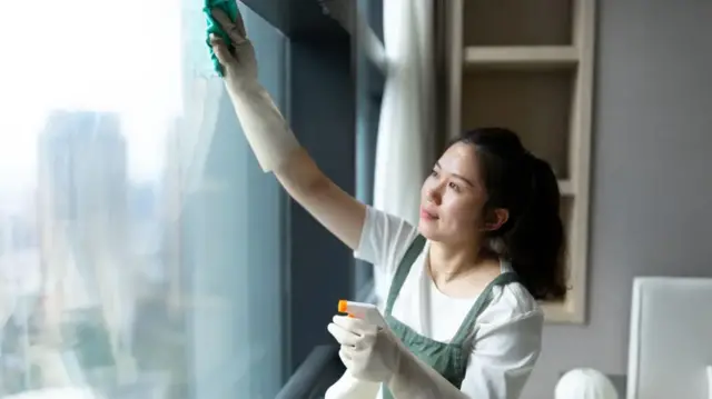 A woman wearing gloves wipes down a window.