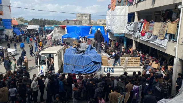 A truck with a large group of people surrounding it distributing Ramadan parcels in March 2024