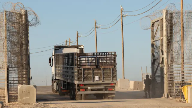 A loaded lorry drives through a gate. The gate has coiled wire round it.