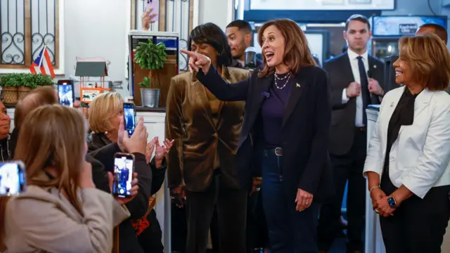 Harris points and grins at someone outside the photo frame as she's surrounded by people taking photos of her in the restaurant