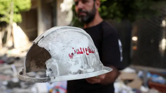 A man holds up a damaged helmet that reads "Civil Defense", following an Israeli strike on central Beirut's Bachoura neighbourhood