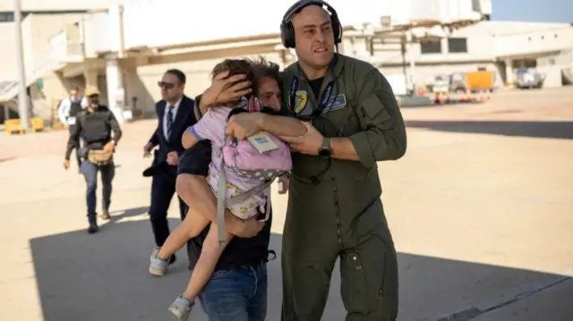 Military person escorts adult and baby on tarmac