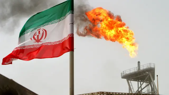 A file photo of an Iranian flag in front of a flame from an oil flare